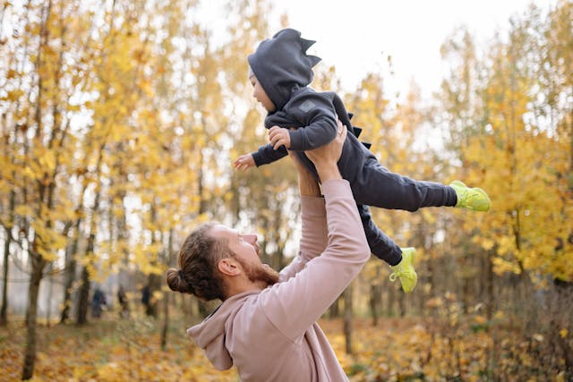 A man holds a toddler high in the air on a fall day.