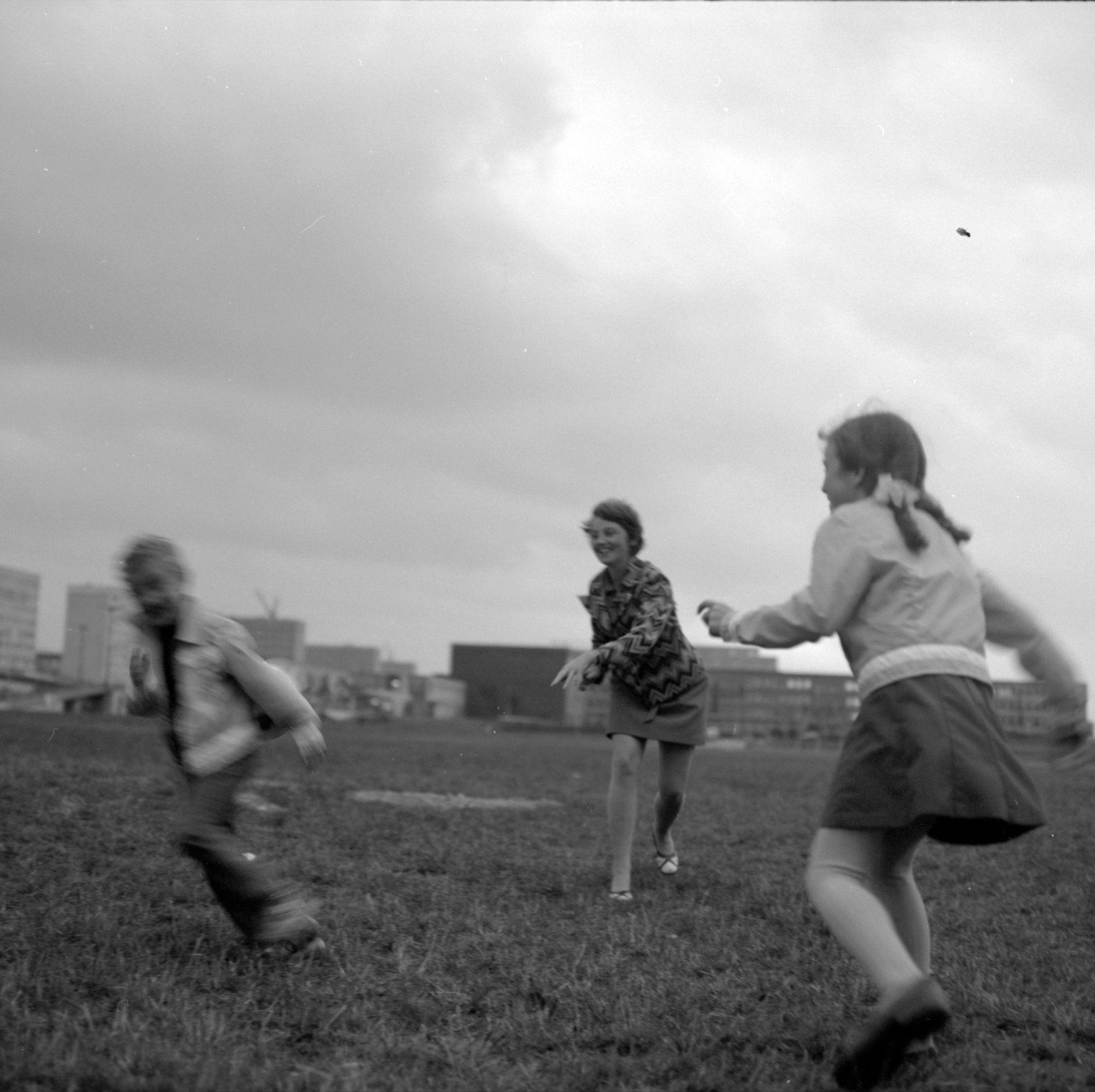 Three children playing in a grassy area, with each partially blurred showing they are moving as they play together.