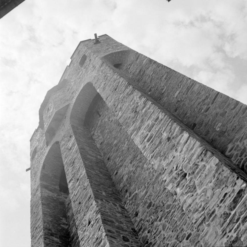 stone tower with arched openings, viewed from below against a partly cloudy sky.