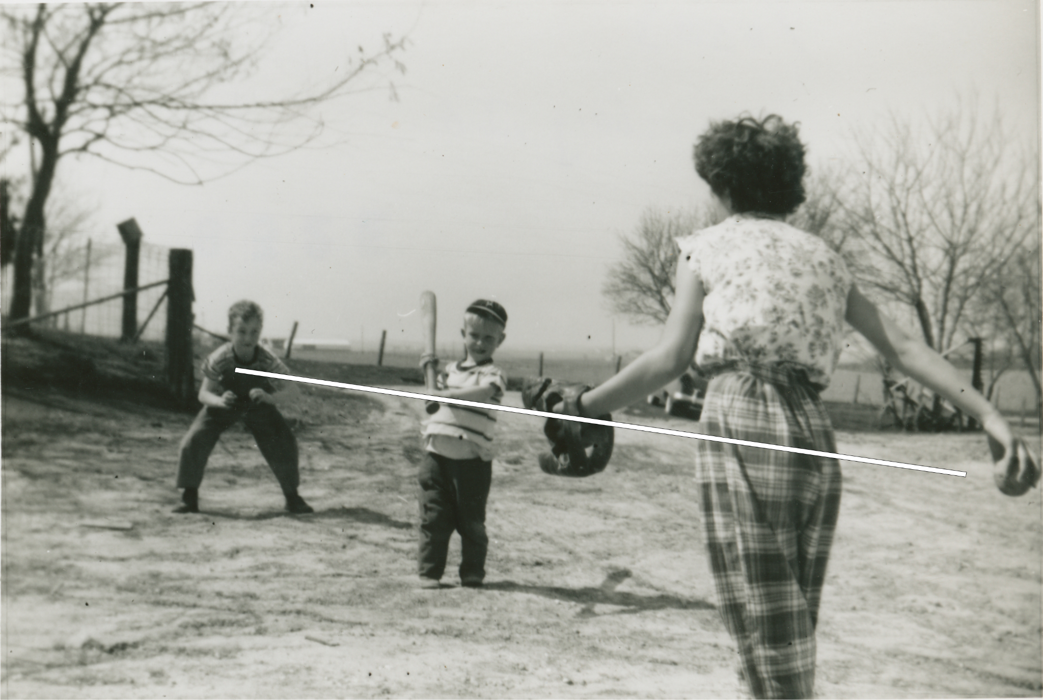 A woman with back toward camera prepares to throw a baseball to a small bow holding a bat, with another boy behind the batter as the catcher. A white line connects the 3 figures.