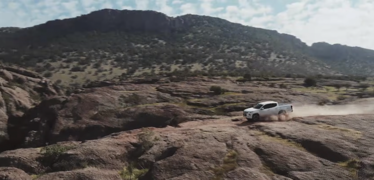 A white pickup truck moving along a hilly dirt path toward the left of the photo, with dust billowing behind.