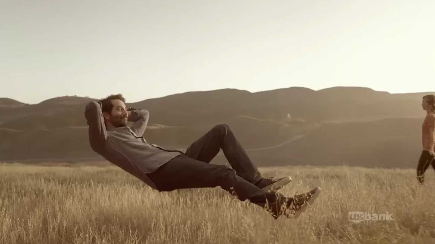 A man leaning back and cradling his head in his hands, appearing to levitate above a field.