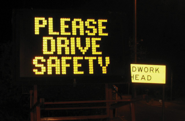 A lit up road sign saying “Please Drive Safety”
