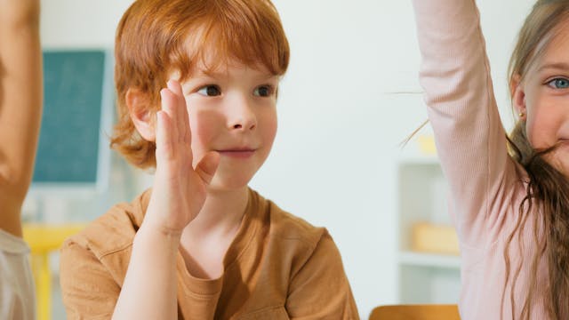 A red-haired boy timidly raises his hand.