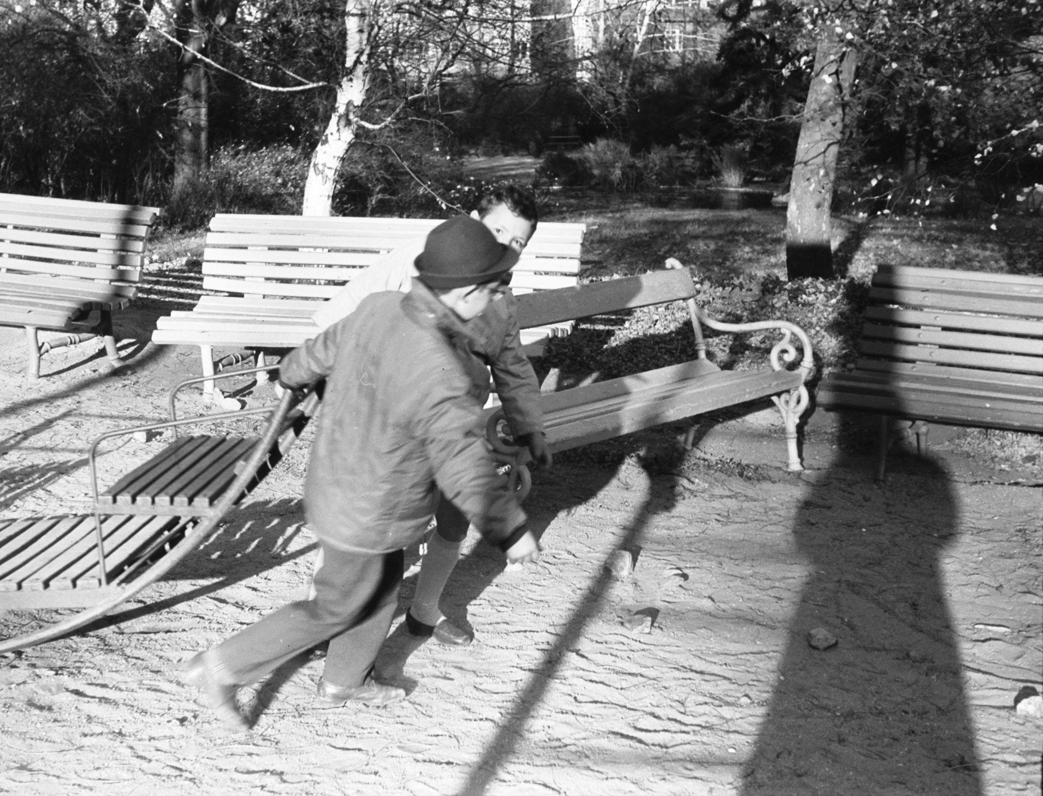 2 young boys in coats running and pulling a sled nearby some park benches.