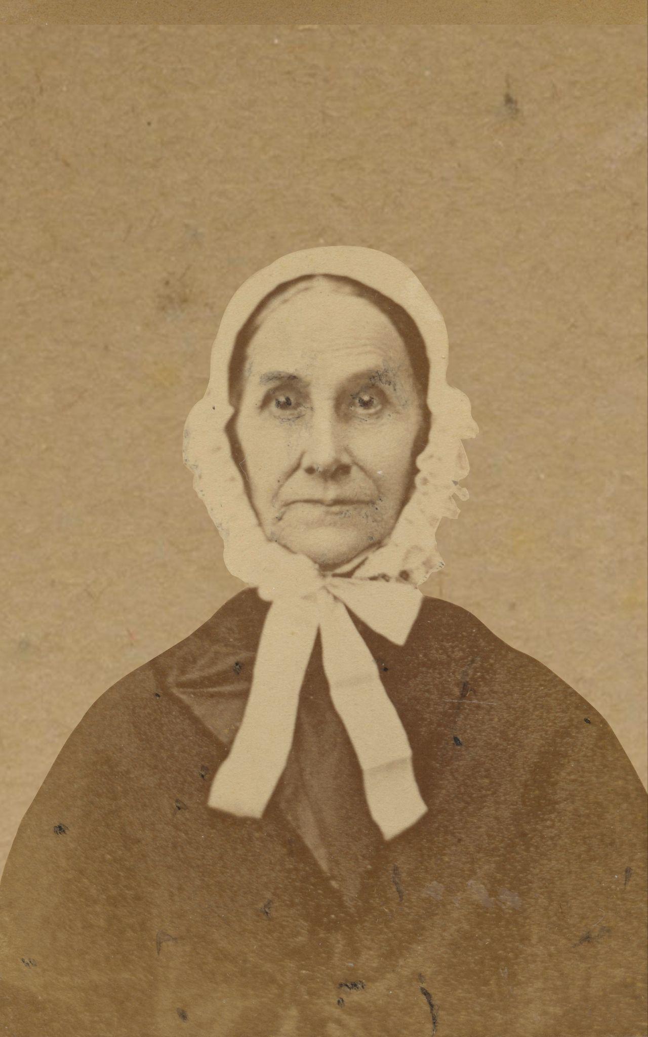 An historic black &amp; white photo of a serious-faced woman wearing a light-colored bonnet and starting straight at the camera.
