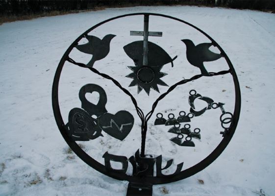 a circular metal sculpture with doves, hearts, a cross, and other symbols