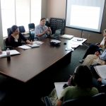 seven people sitting around a table talking and taking notes