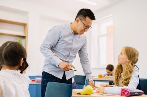 A teacher talks to a student while other students work at their desks.