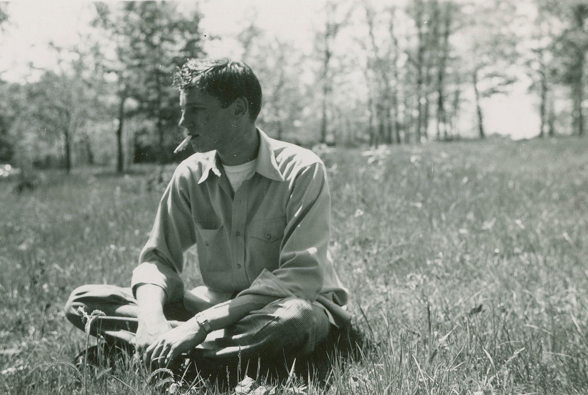 A young man sitting in a field with a cigar in his mouth.