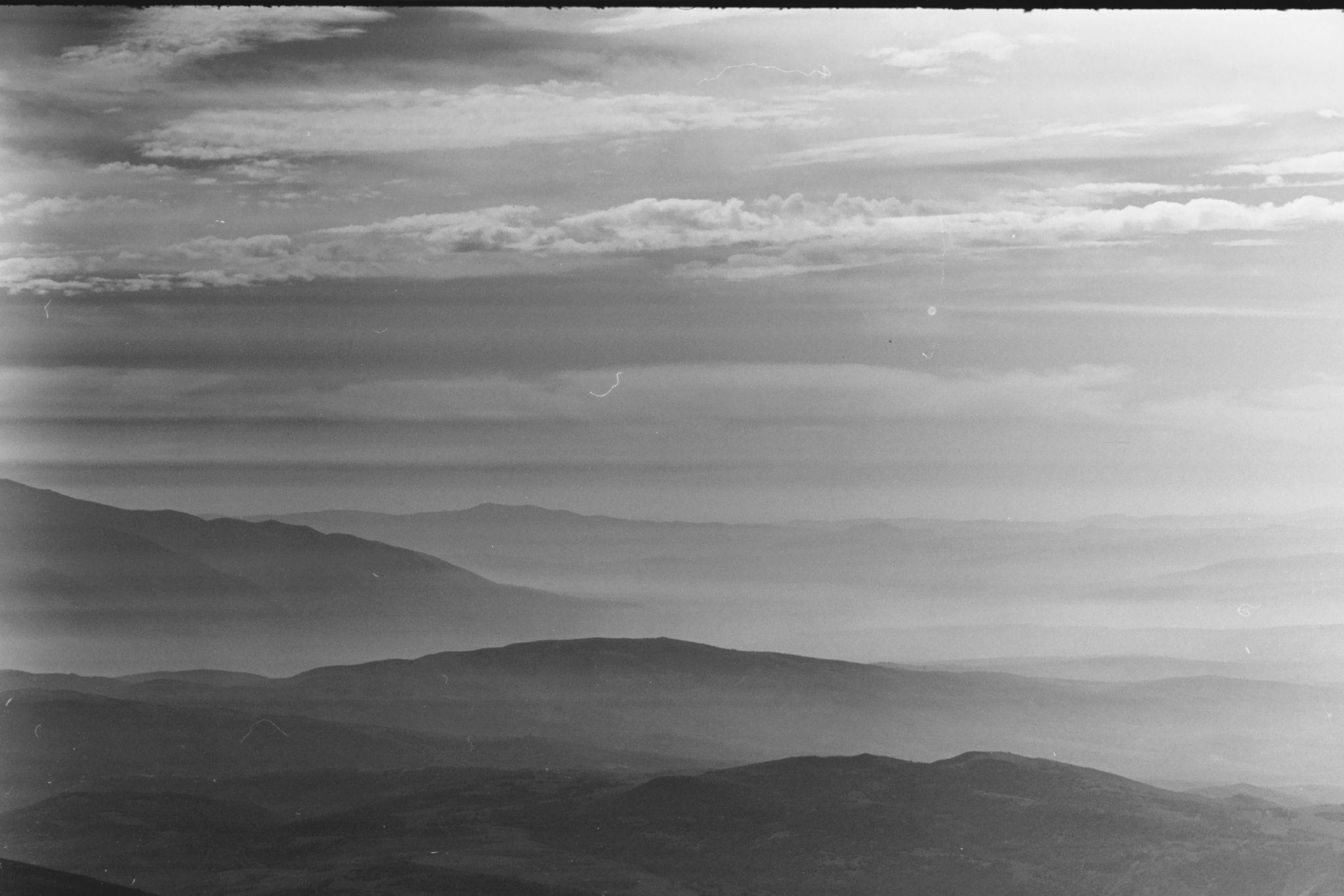A landscape with low, fog-covered hills and horitonzal clouds in the background.