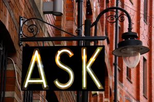 an illuminated street sign that reads "ask"