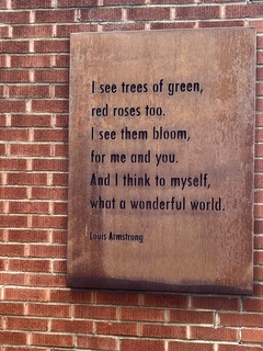 Image of a plaque on the Louis Armstrong House Museum with the lines of "What a Wonderful World": I see trees of green, red roses too, I've seen them bloom for me an you. And I think to myself, what a wonderful world." -Louis Armstrong