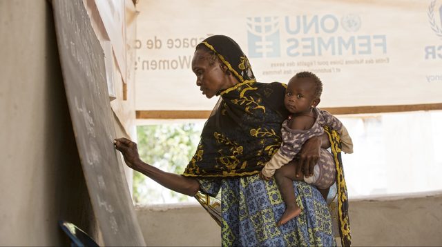 Refugee from Cameroon holds her granddaughter while taking an adult education class
